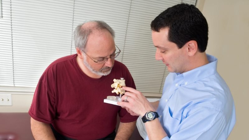 Therapist discussing a spine model with an older patient